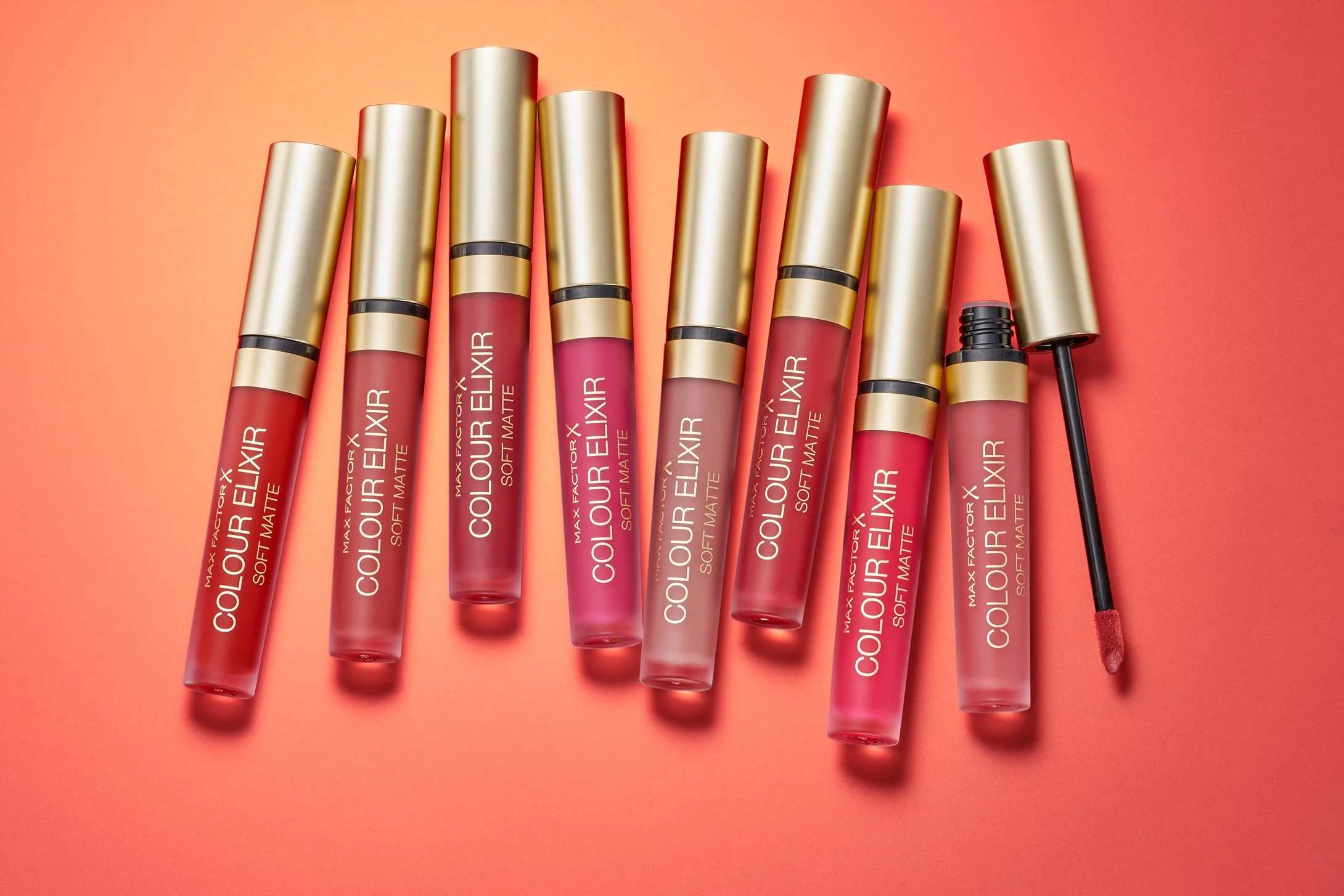 lip gloss makeup products in still life composition . collection of reds on orange background 