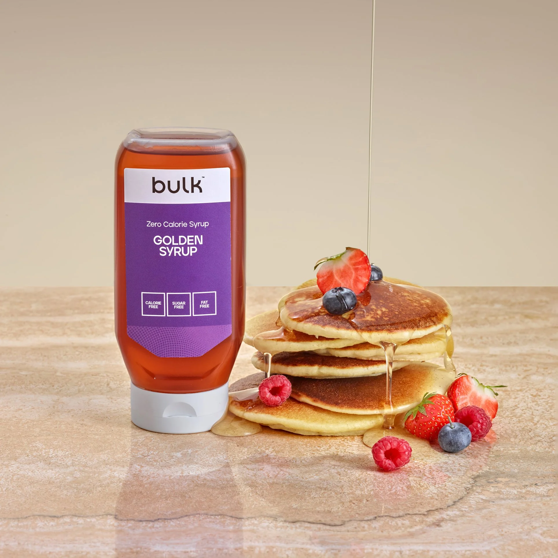 Bulk golden syrup photographed with pancakes and fresh fruit for commercial food photography.