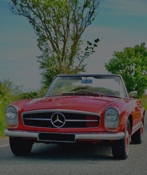 Front view of a classic red Mercedes-Benz convertible car parked outdoors with trees and a blue sky in the background.