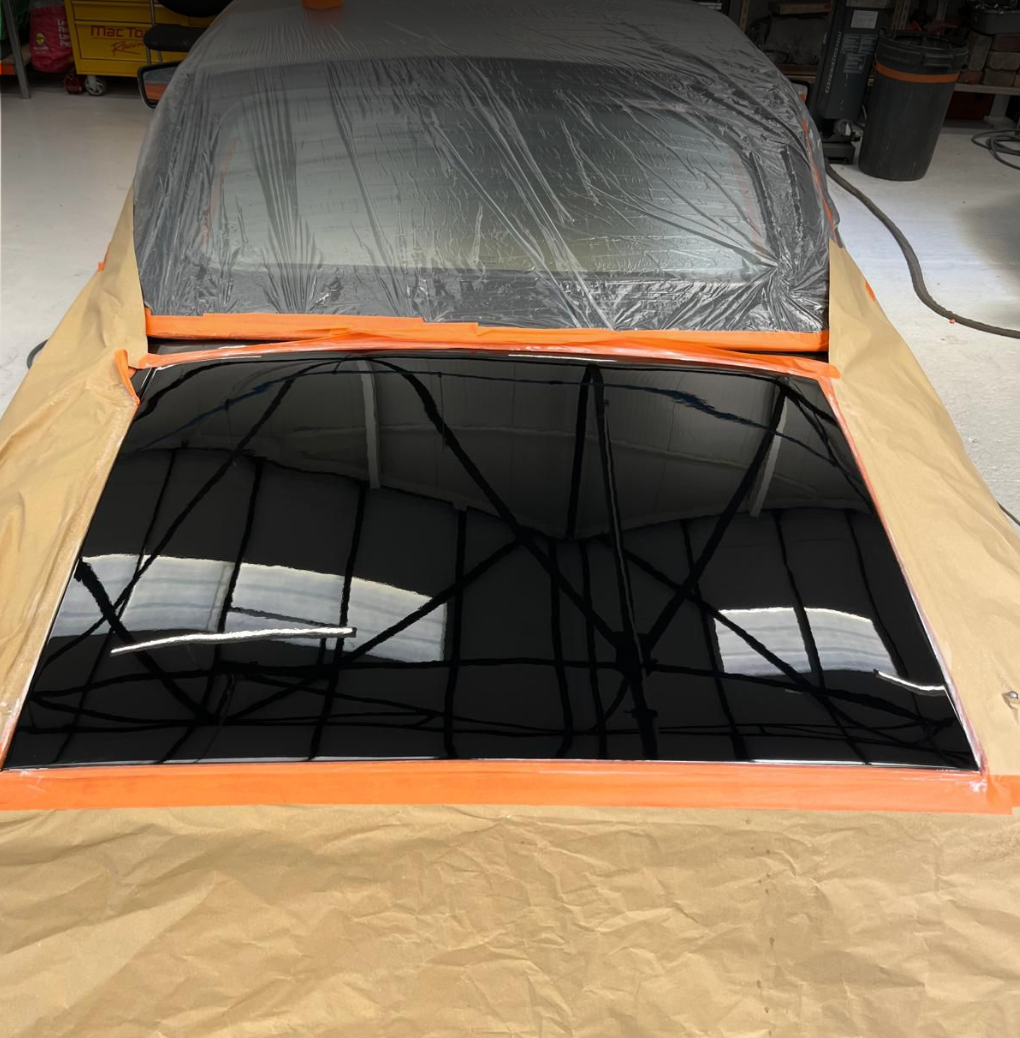 Reflective black car windshield with masking tape and plastic covering the edges, in a garage or workshop.