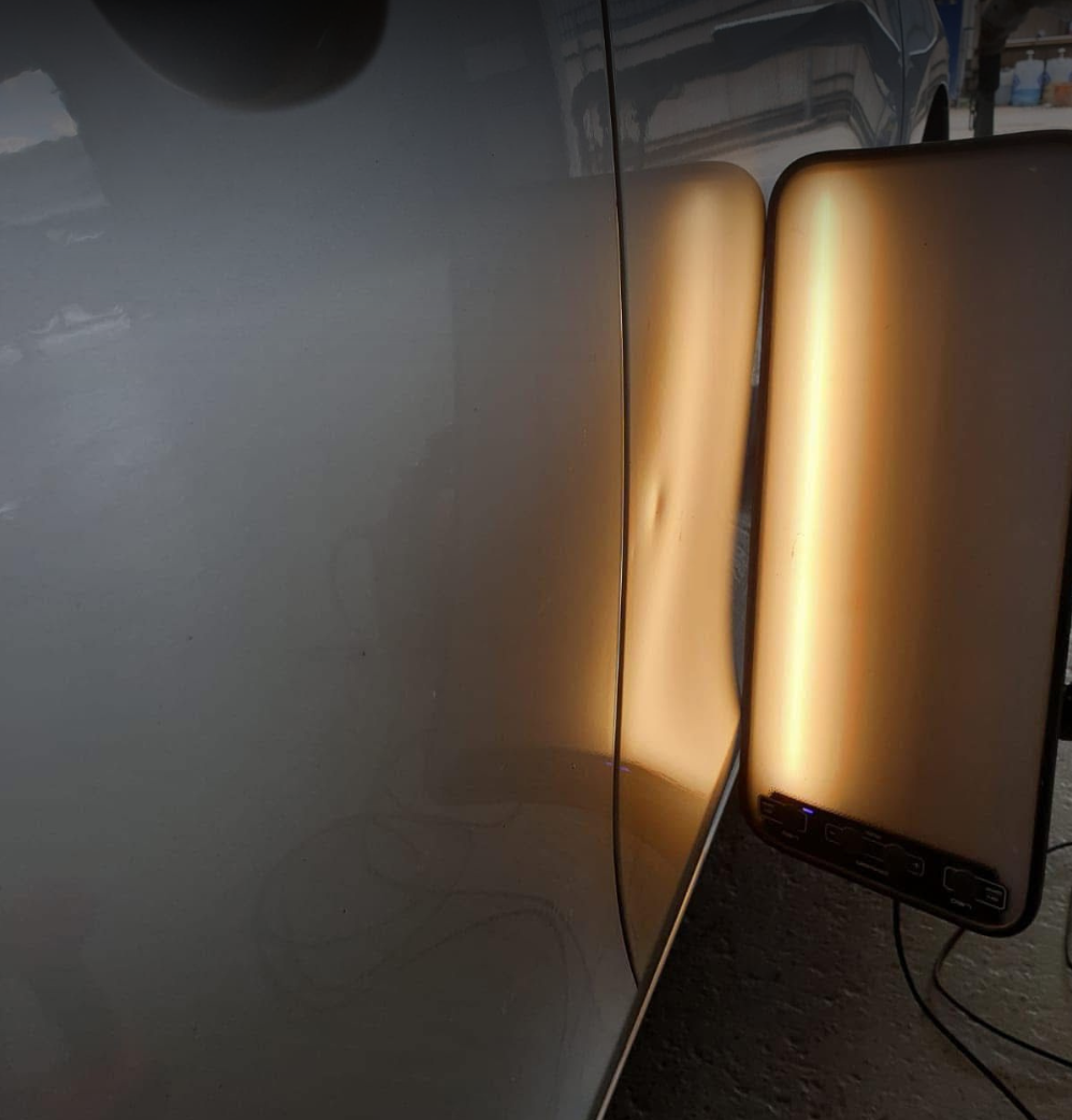 Close-up of a reflective surface showing a mirror and a beige-colored object or surface reflected in it, with visible electrical cords.