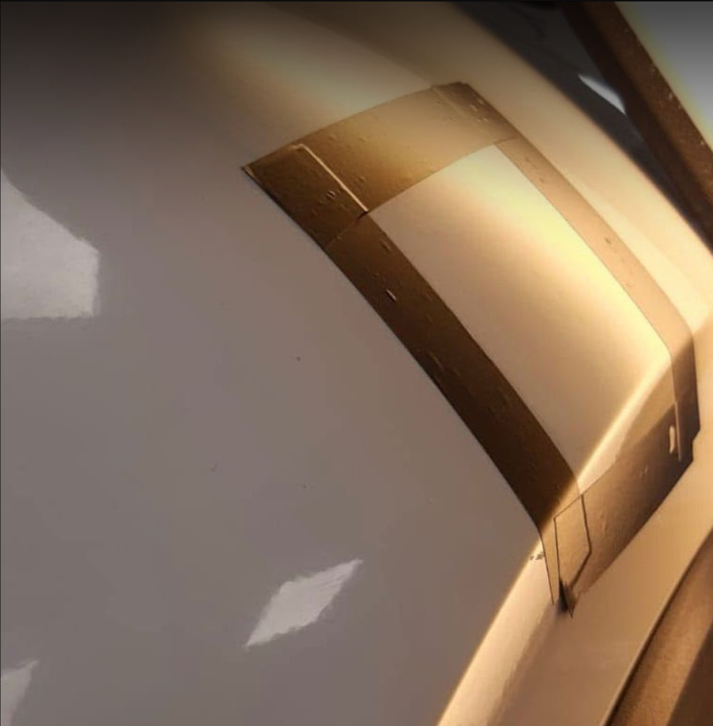 Close-up of a metallic, gold-colored object with a curved surface, possibly a vehicle or piece of machinery, with reflections and a white background.