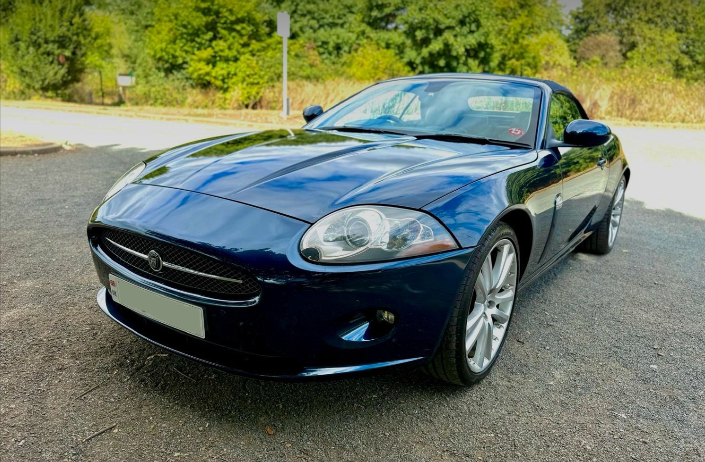 A black convertible sports car parked on a gravel surface with green trees and bushes in the background.