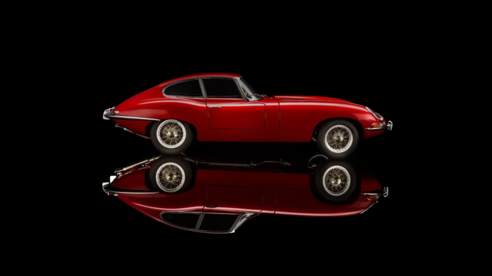 A vintage red sports car on a black background with a mirror reflection underneath.