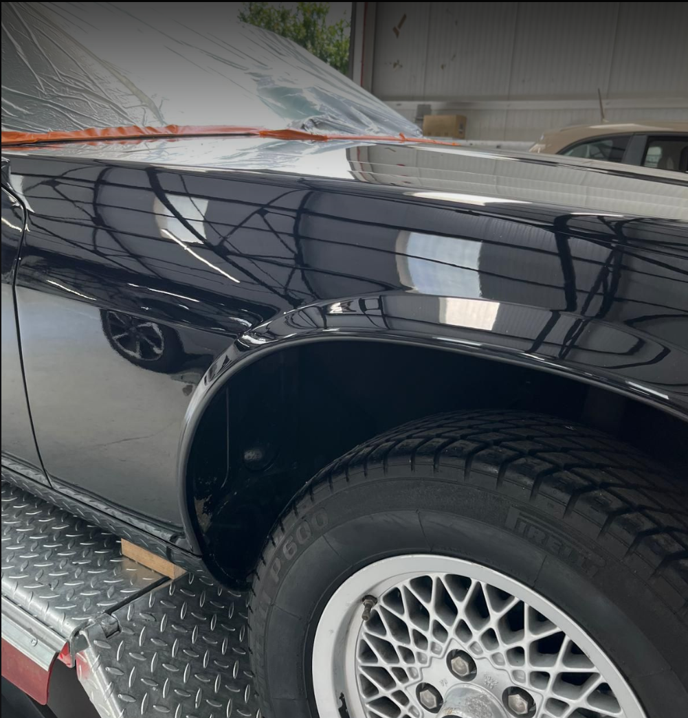 Close-up of a car's black body and wheel, parked on a metal platform inside a garage or warehouse.