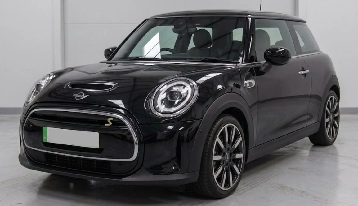 Black Mini Cooper car parked indoors with a white wall background.
