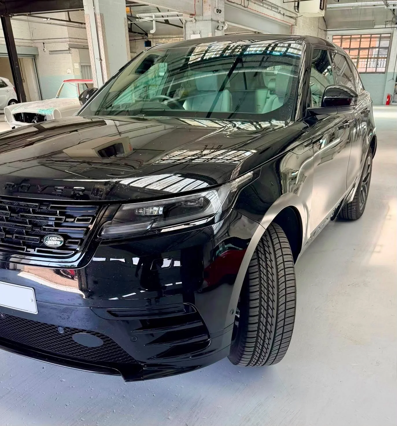 A black Range Rover parked inside a spacious garage or warehouse, with several other vehicles visible in the background.