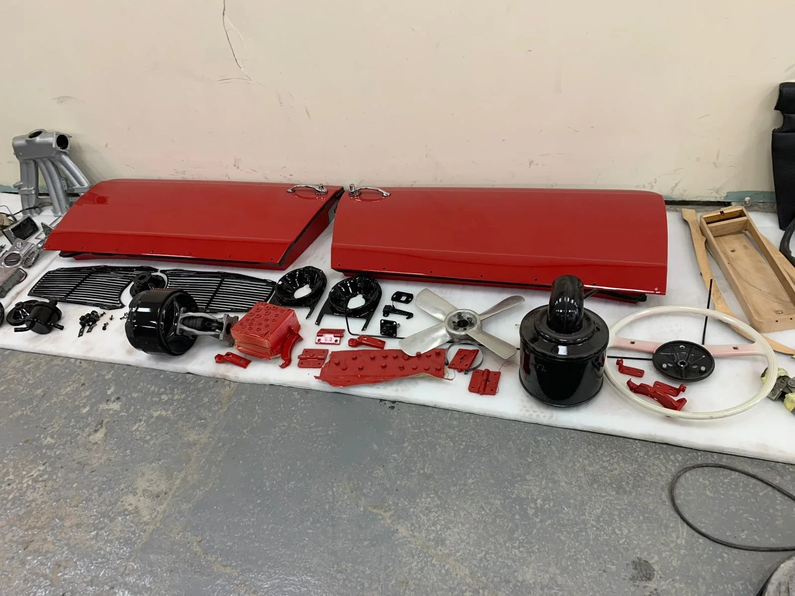 Disassembled vintage red train engine parts laid out on a white sheet, including two large red side covers, a black motor, a silver fan, various small red and black components, and a wooden tray on the side.