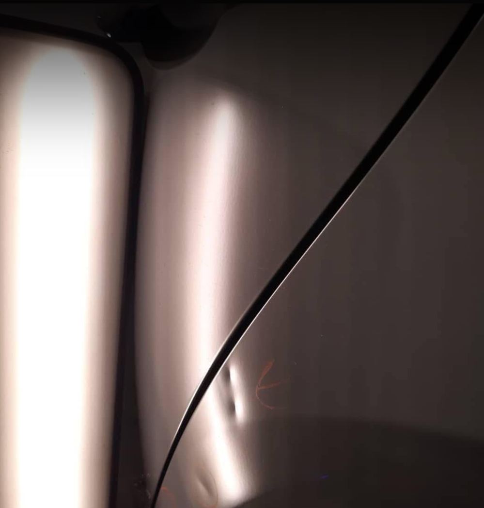 Close-up of a reflective metallic surface with dark curved lines and soft lighting creating highlights and shadows.