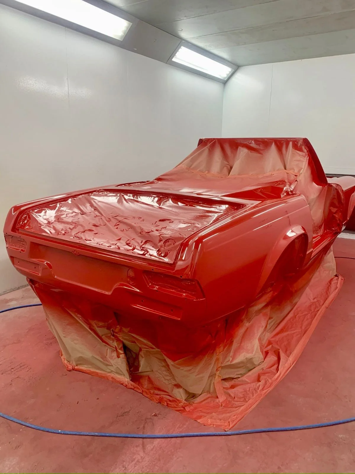 A red car model in a paint booth, partially covered with protective paper and plastic for repainting.