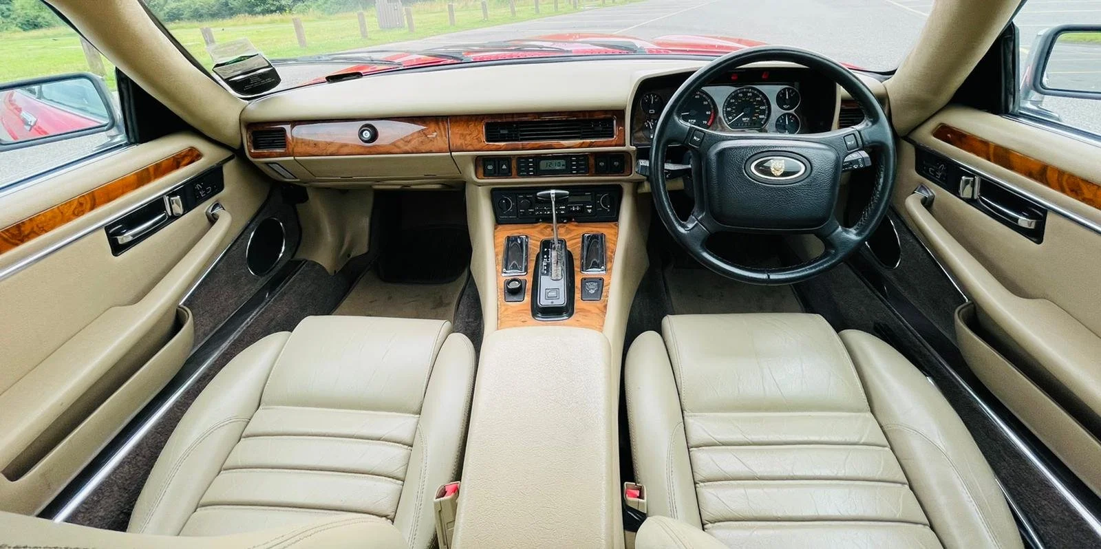 Interior of a classic luxury car with beige leather seats, wood trim, and a dashboard with analog gauges, steering wheel, and center console with gear shift and controls.