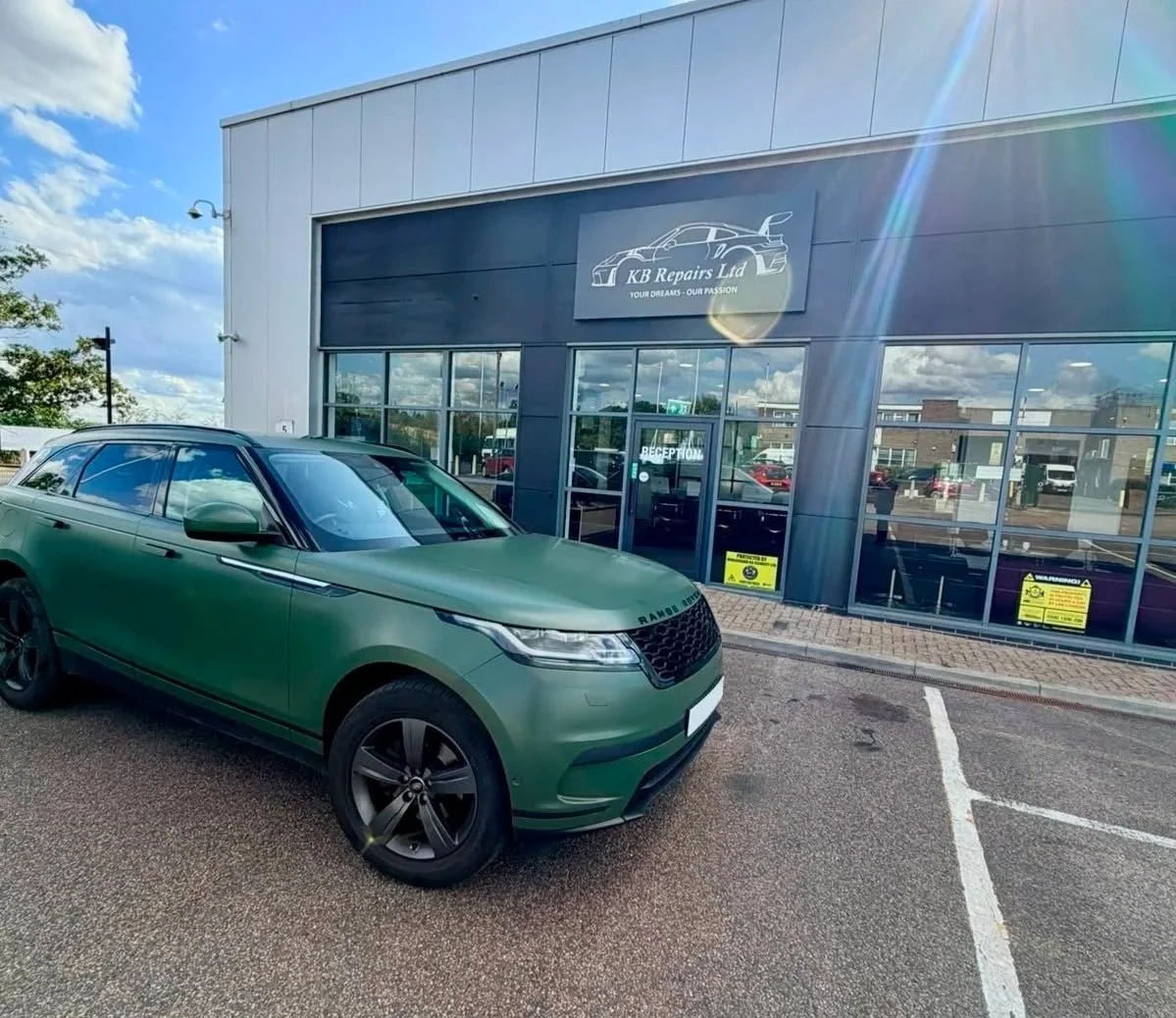 Green Range Rover parked outside KB Repairs Ltd auto repair shop with a modern building facade, large windows, and a sign with a line drawing of a sports car.