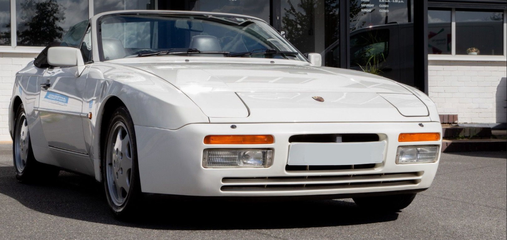 White Porsche sports car parked outside building with shop front and sign.