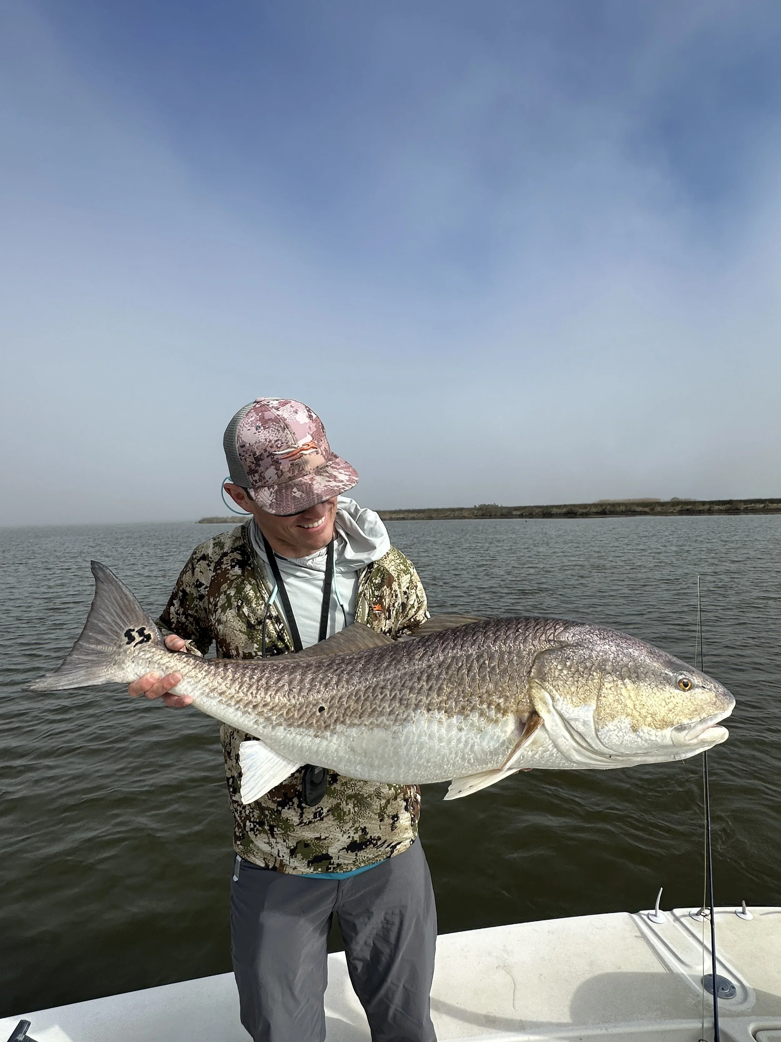“Fishing guide helping guest land a redfish in shallow Louisiana marsh.”