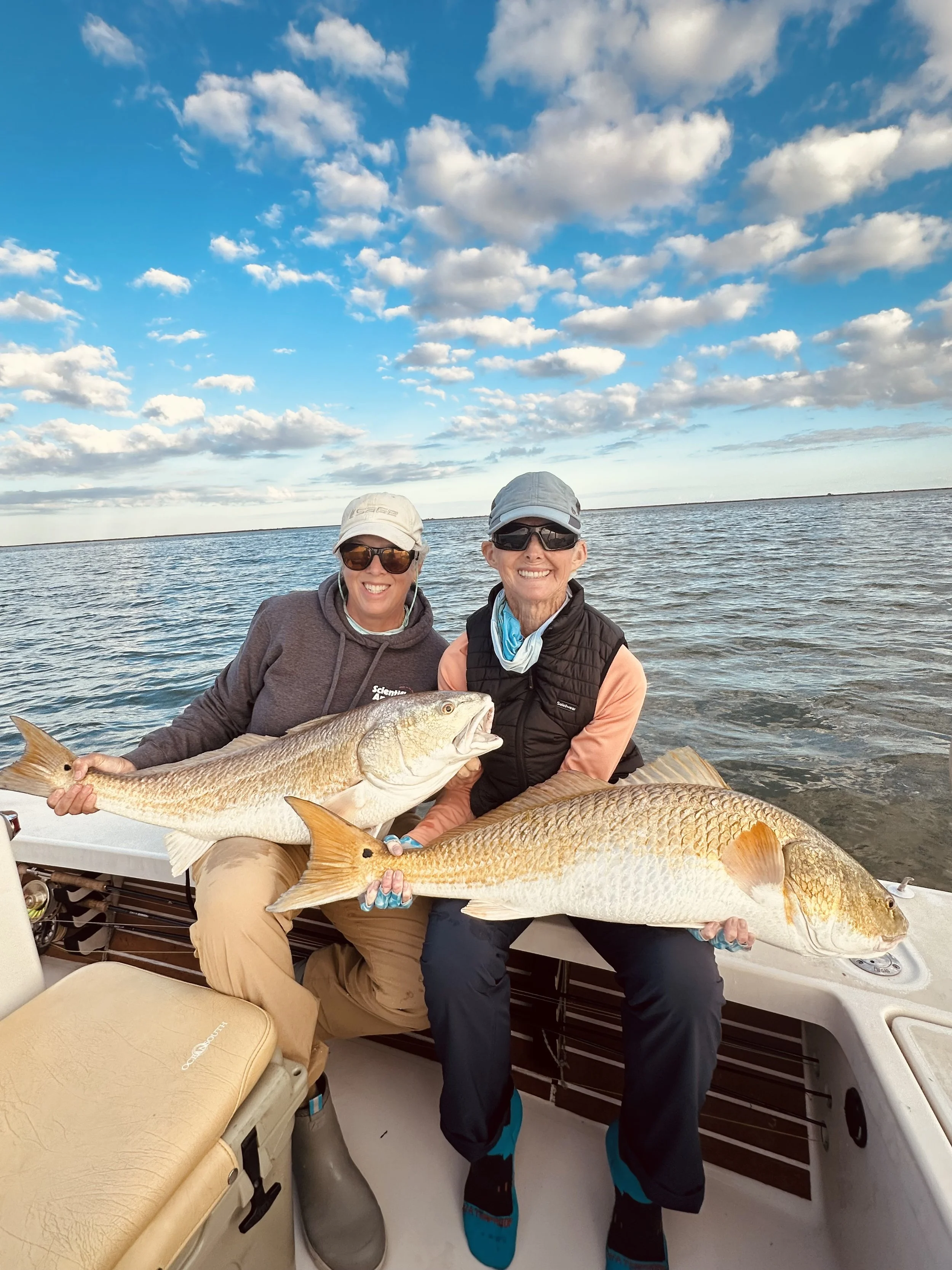 Anglers holding  large Louisiana redfish on an inshore fishing charter in coastal marsh waters.