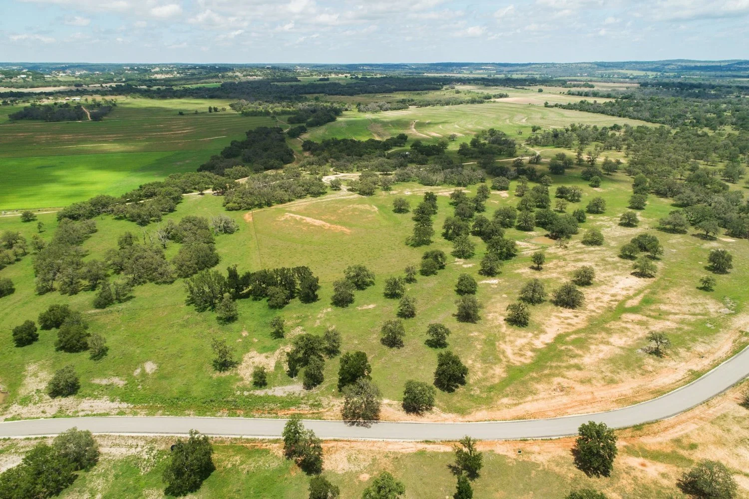 Drone photo of a new paved road winding through mature oak trees on Homestead 24, a Hill Country homesite in Fredericksburg, TX