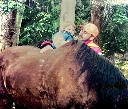 Man and child with brown horse in forested area