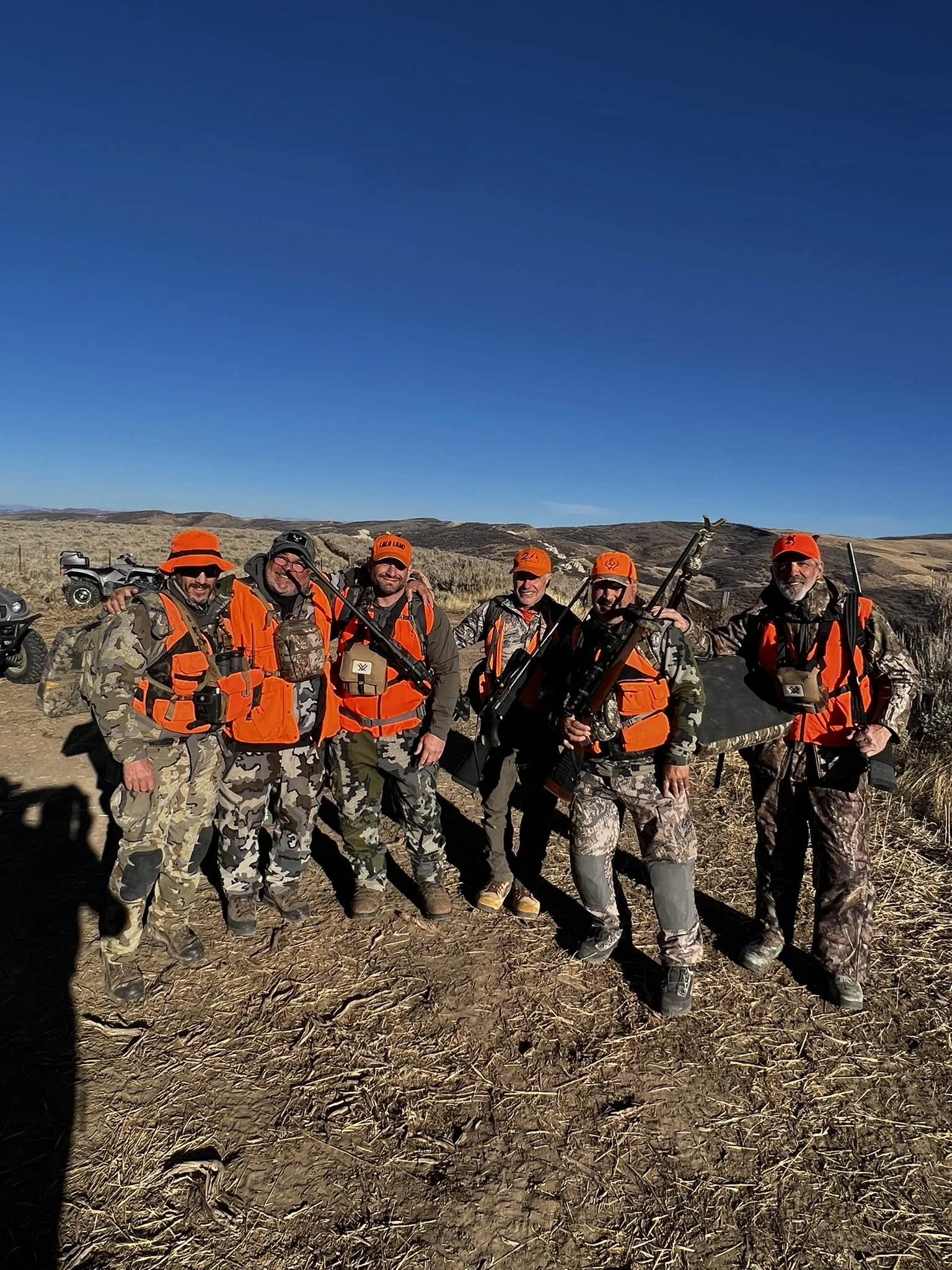 Group of hunters wearing camo and orange gear, standing in a field