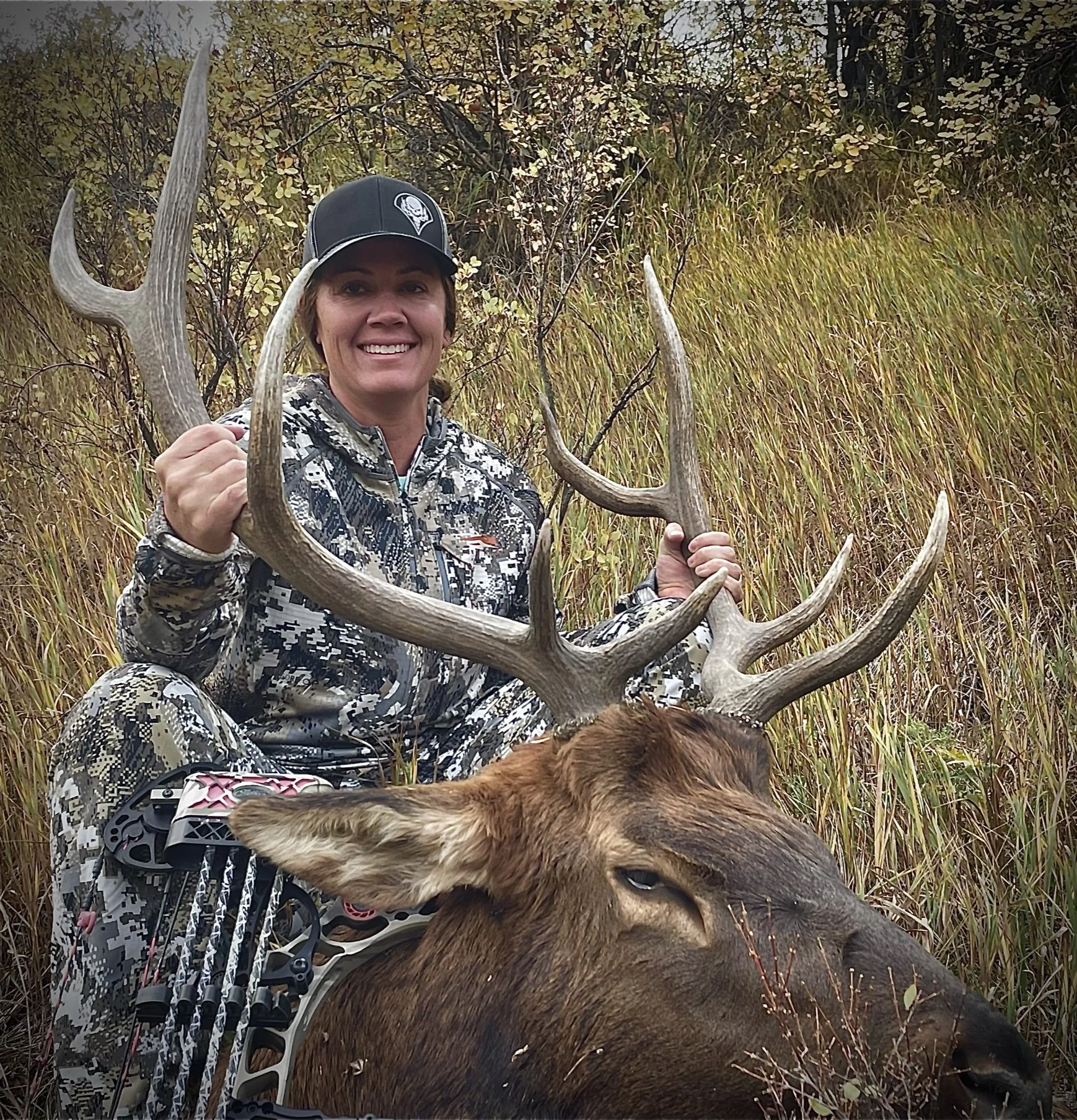 Person in camouflage holding elk antlers in grassy field