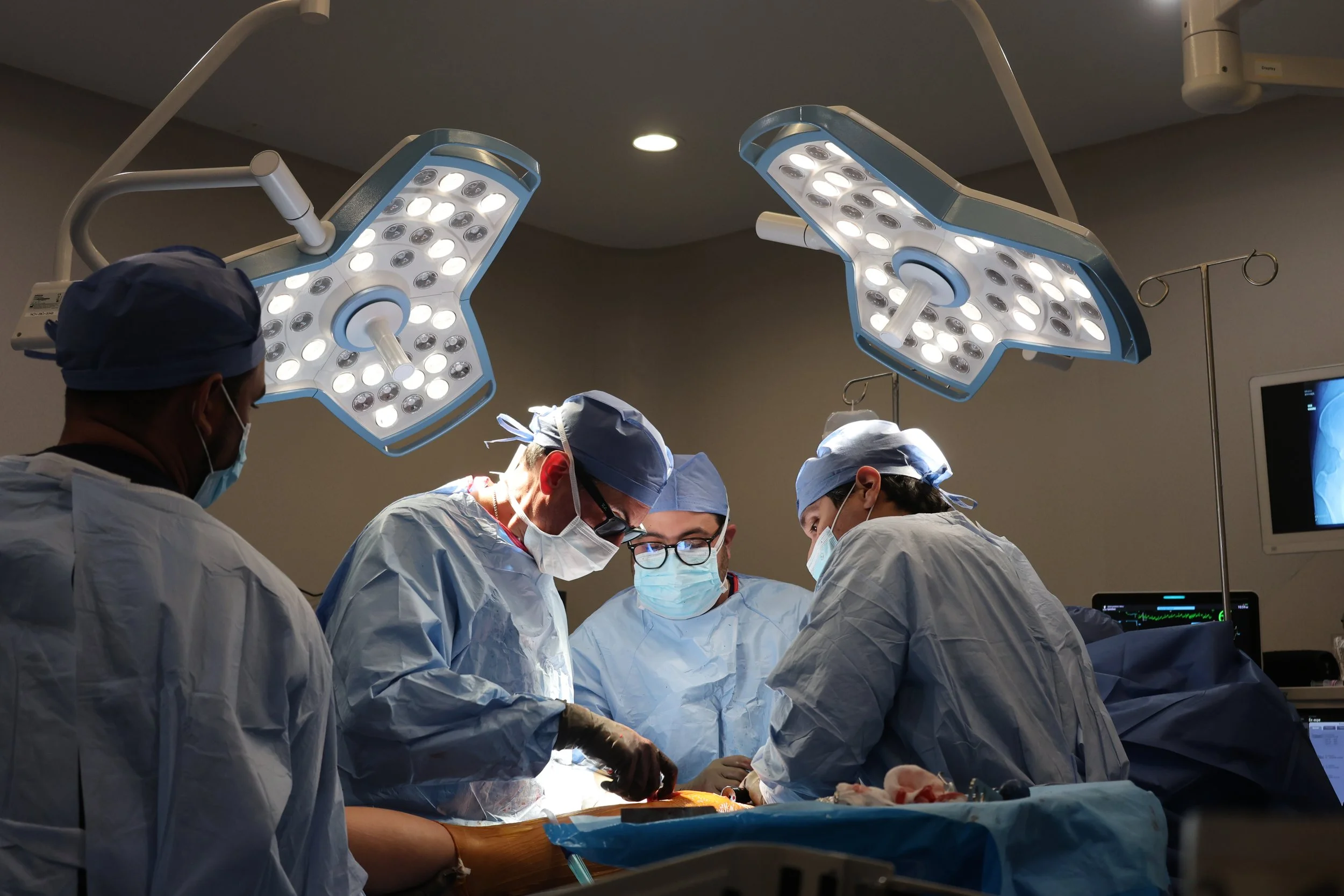 Medical team performing surgery in an operating room under bright surgical lights.
