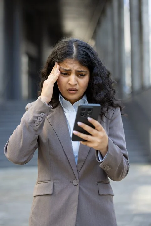 Woman motions with hand as if she has a headache as she reads her mobile phone