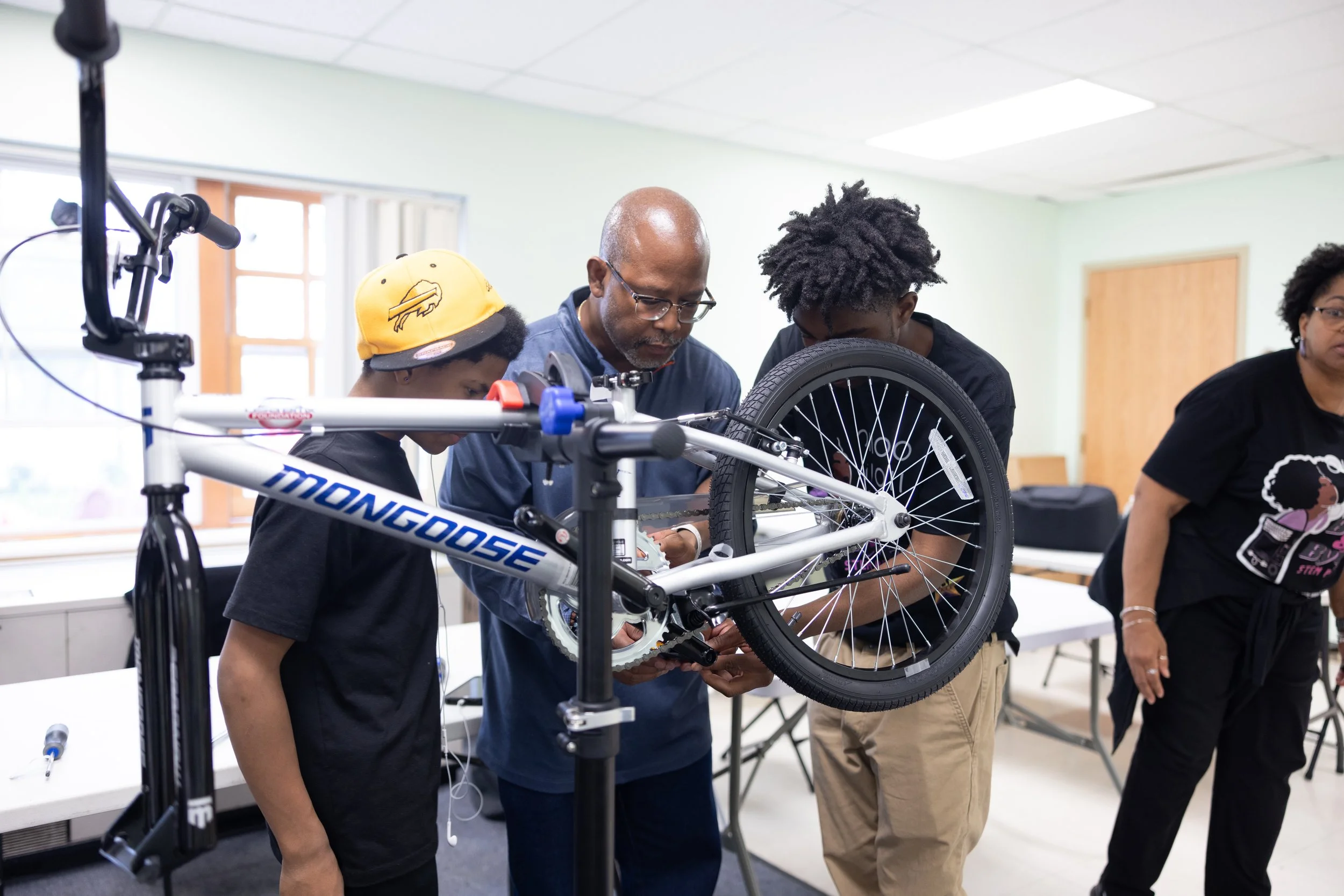 Build-A-Bike 5/29/25 — Older man helping two teens build a bike