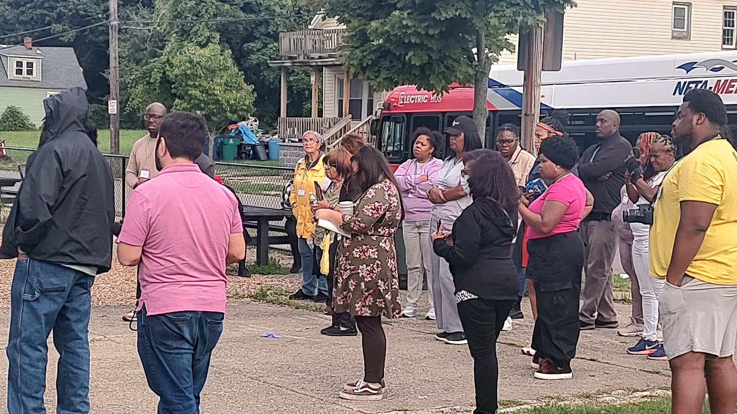 An image of a group of people standing on pavement in front of a NFTA electric bus.