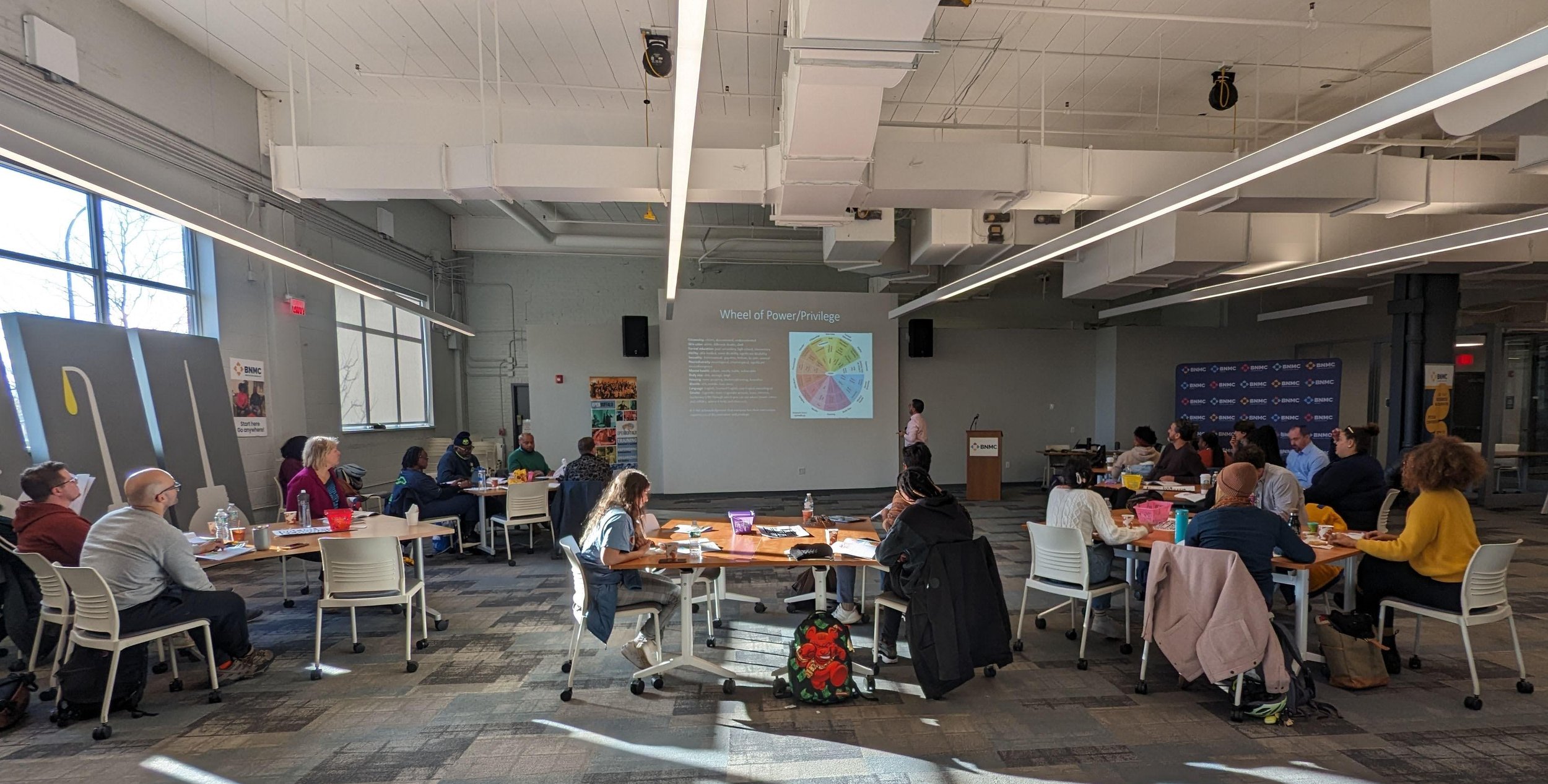 Race, Power, and Privilege Training 11/2/23 — A group of people sitting in a room listening to a presenter speak to the Wheel of Power/Privilege. 