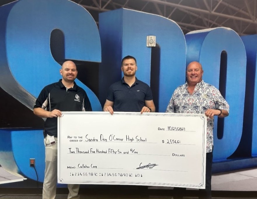 Three men standing indoors in front of large blue letters, holding a giant check made out to Sandra Day O'Connor High School for over $2,500.
