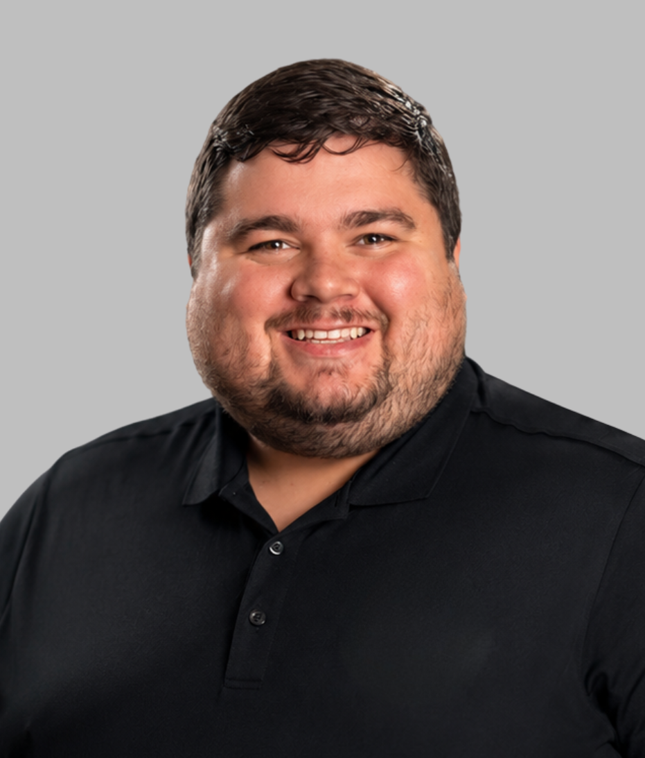 A smiling man with dark hair and a beard, wearing a black collared shirt, against a light gray background.