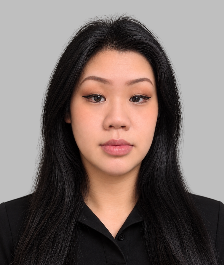 Portrait of a woman with long black hair wearing a black top and a gold necklace with a circular pendant against a gray background.