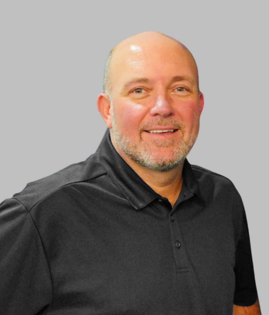 A smiling man with a beard and bald head, wearing a black polo shirt, against a plain light background.