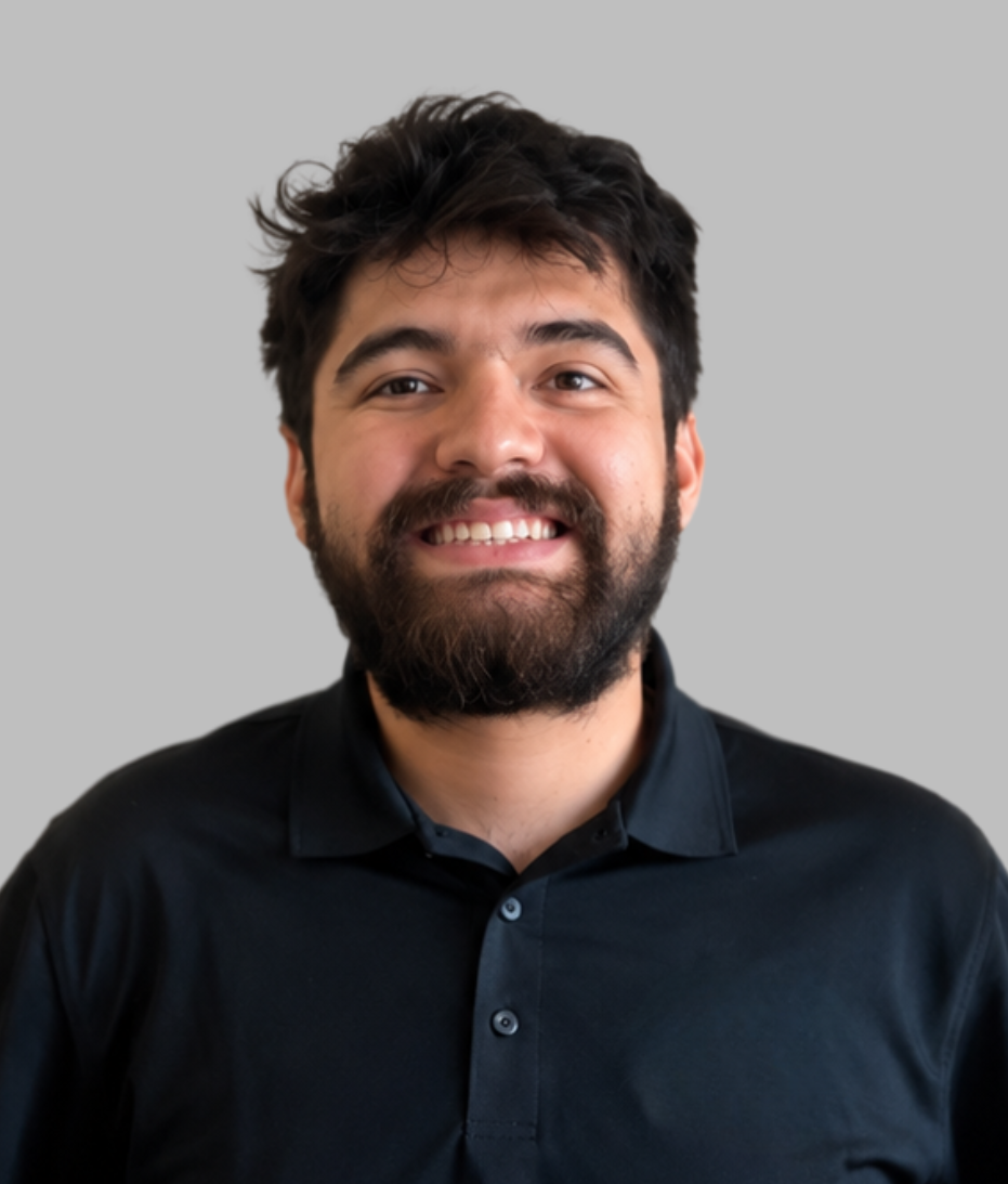 Portrait of a smiling young man with dark hair and a beard, wearing a black collared shirt, against a plain gray background.