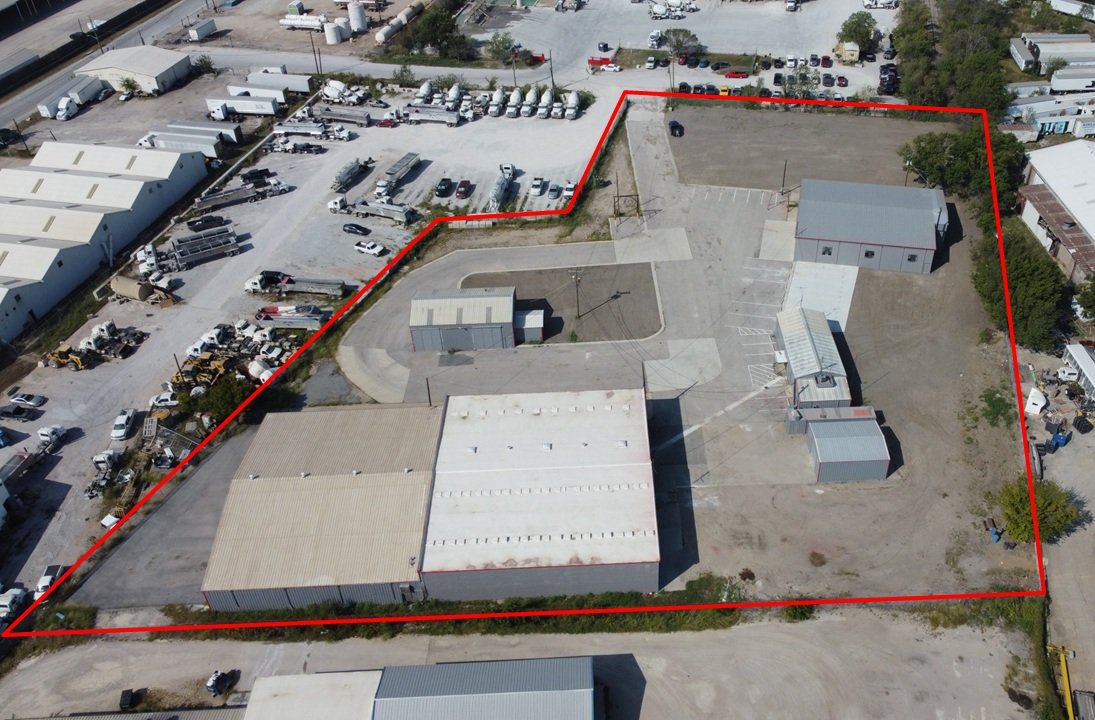 Aerial view of a commercial property outlined in red, with multiple buildings, parking areas, and surrounding lot, situated in an industrial area with other similar properties nearby.
