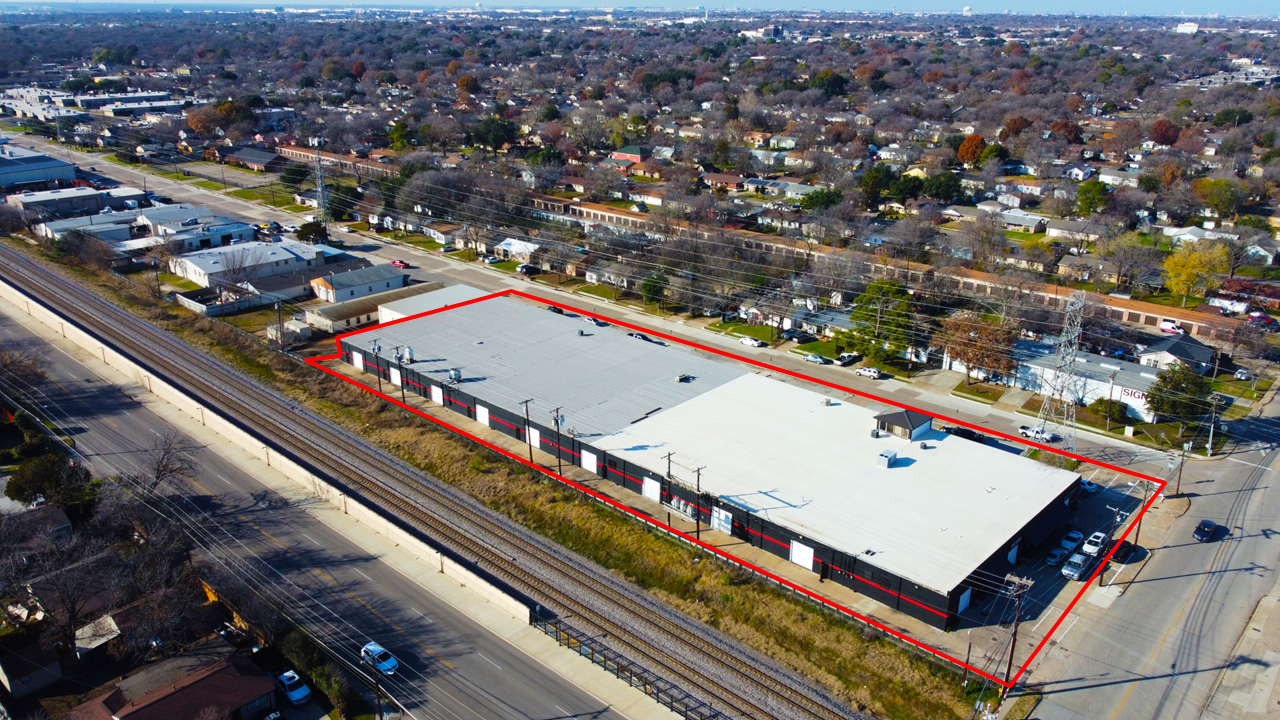 Aerial view of a commercial building with a large flat rooftop, outlined in red, located adjacent to a railway line and surrounded by streets and residential neighborhoods.