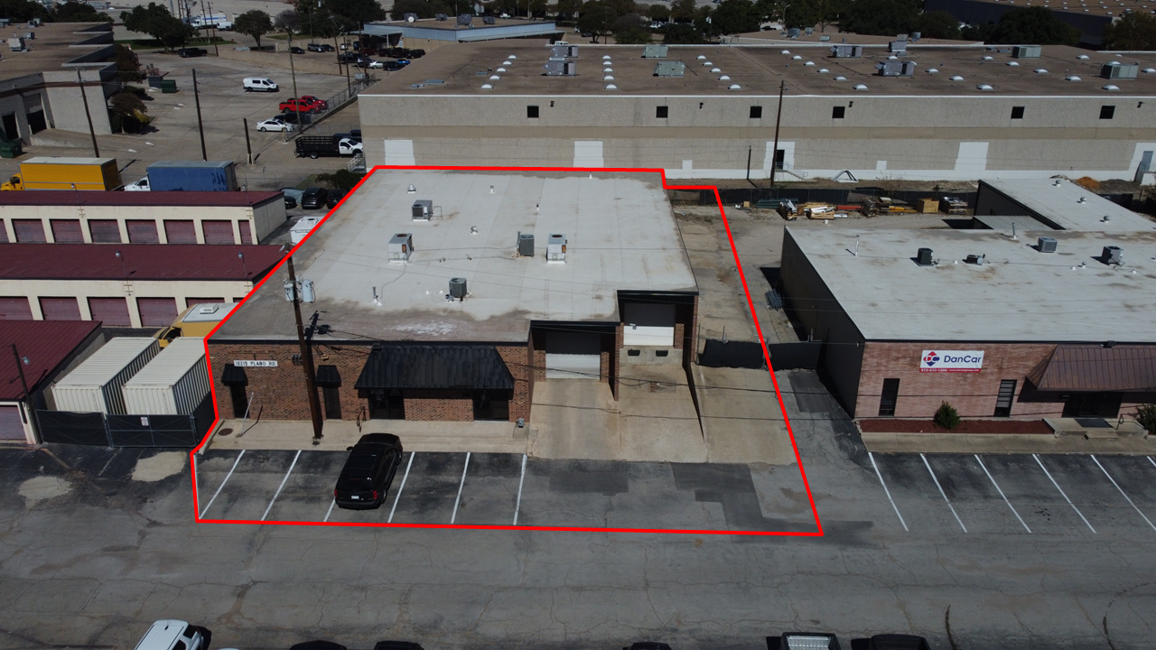 Aerial view of a commercial building with an adjacent parking lot, outlined in red, in an industrial area.