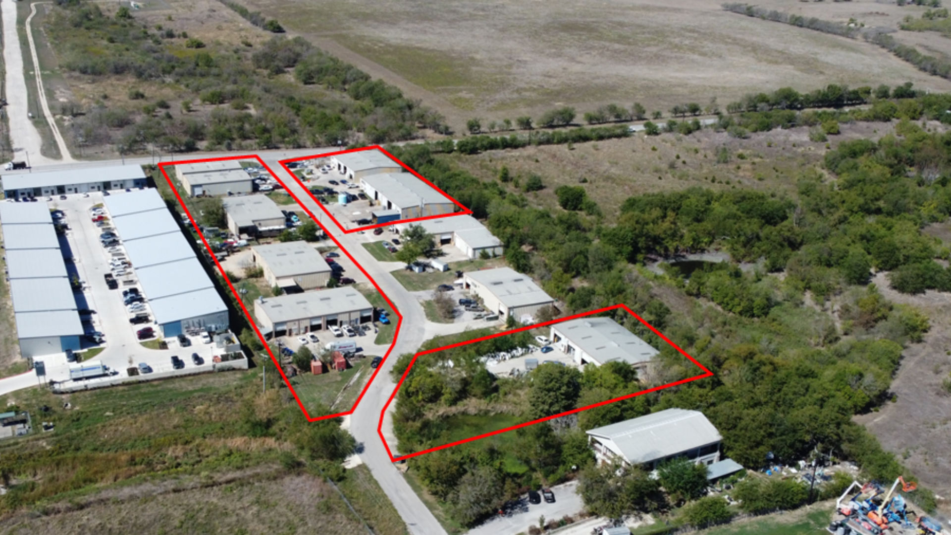 Aerial view of a commercial and industrial complex outlined in red, surrounded by greenery and open land.