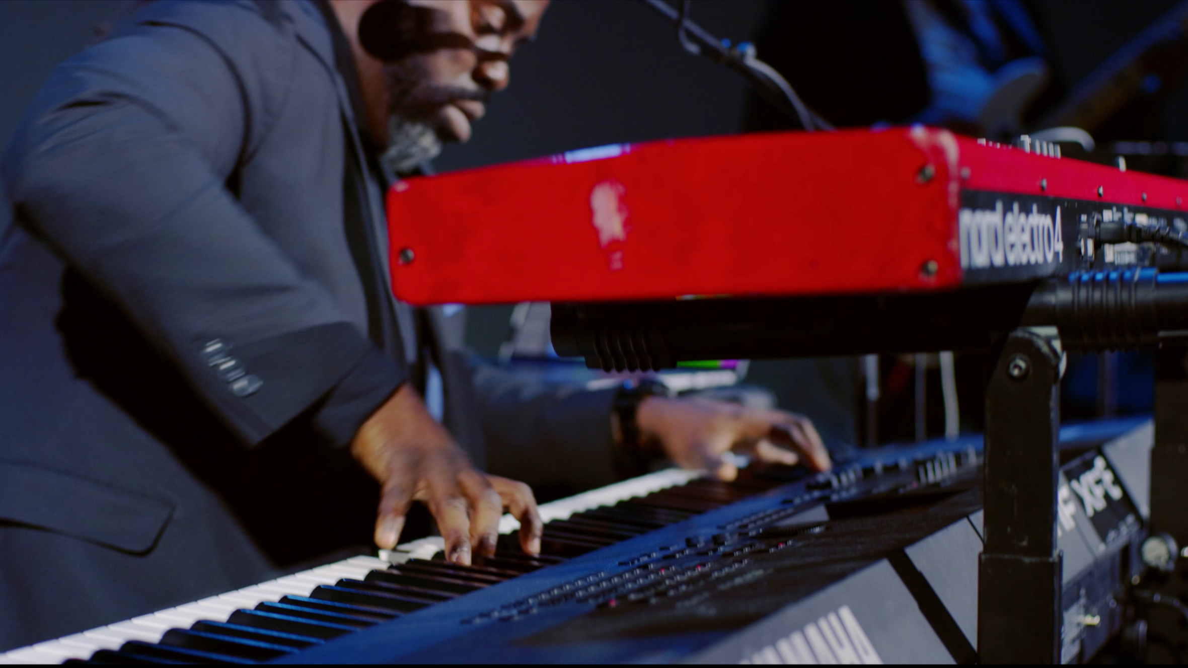 A person playing a keyboard with a red synthesizer above it during a performance.