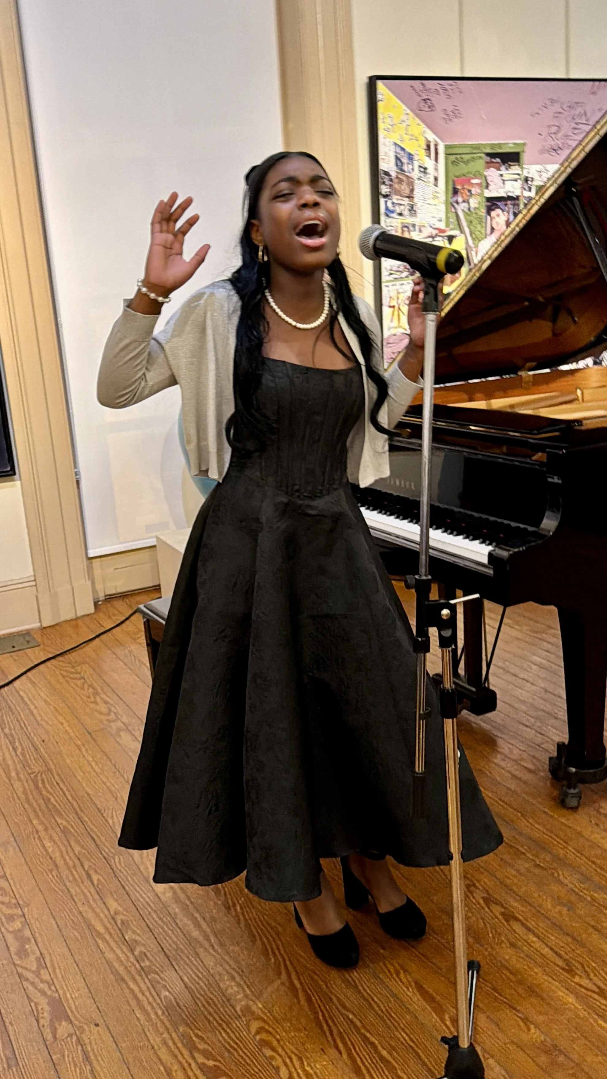 A woman singing passionately while holding a microphone in front of a grand piano.