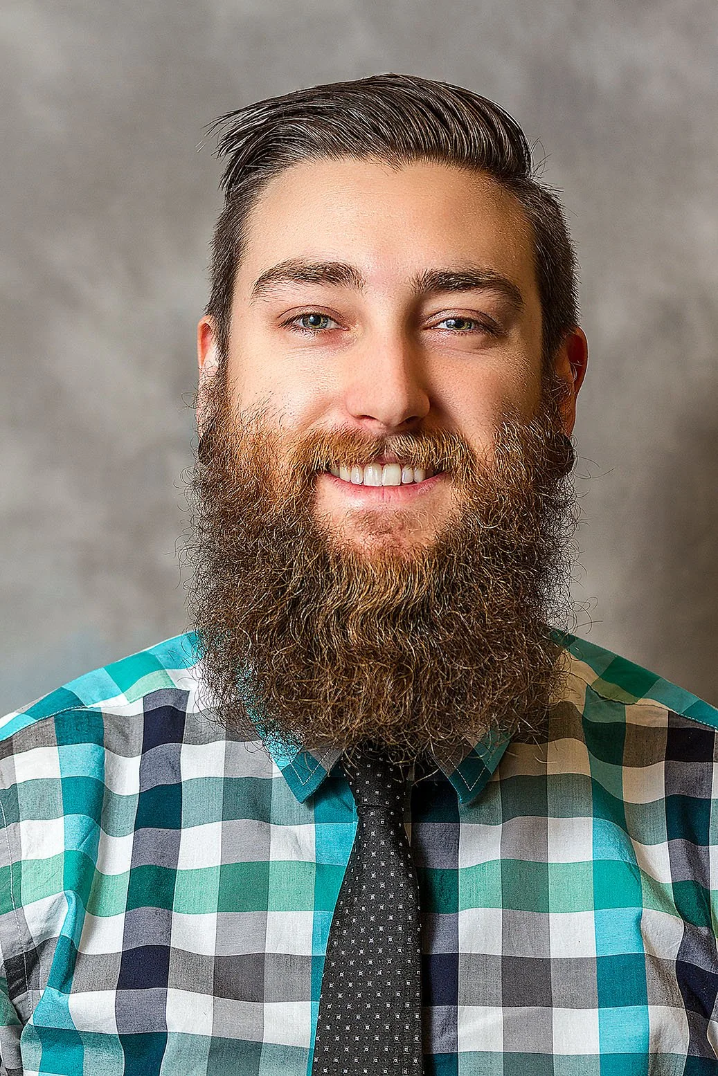 Smiling man with a beard in a checked shirt and tie, photographed in the studio