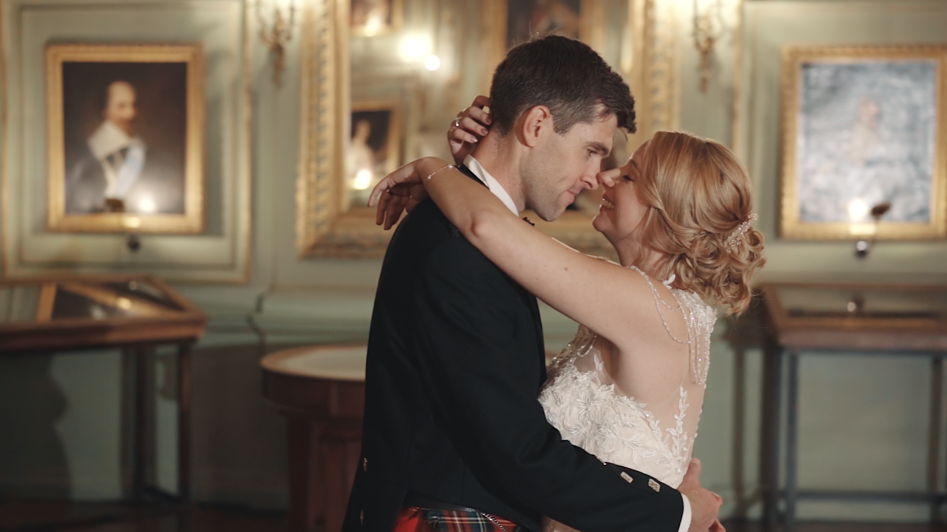 A couple dancing closely in an elegant room with antique portraits and mirrors on the walls.