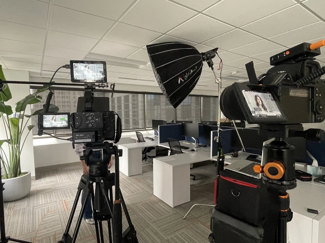An office setup with multiple cameras and lighting equipment in front of desks and chairs.