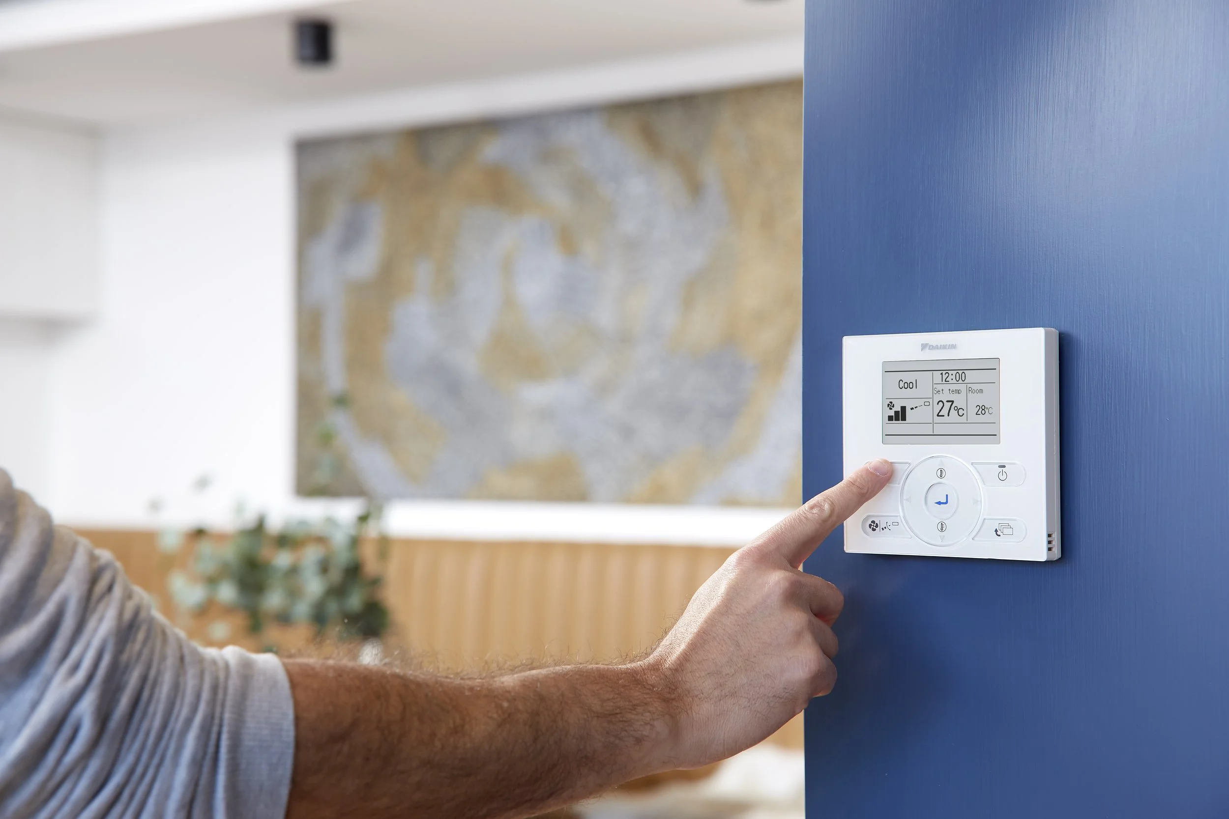 Person adjusting a thermostat on a blue wall in a living room.