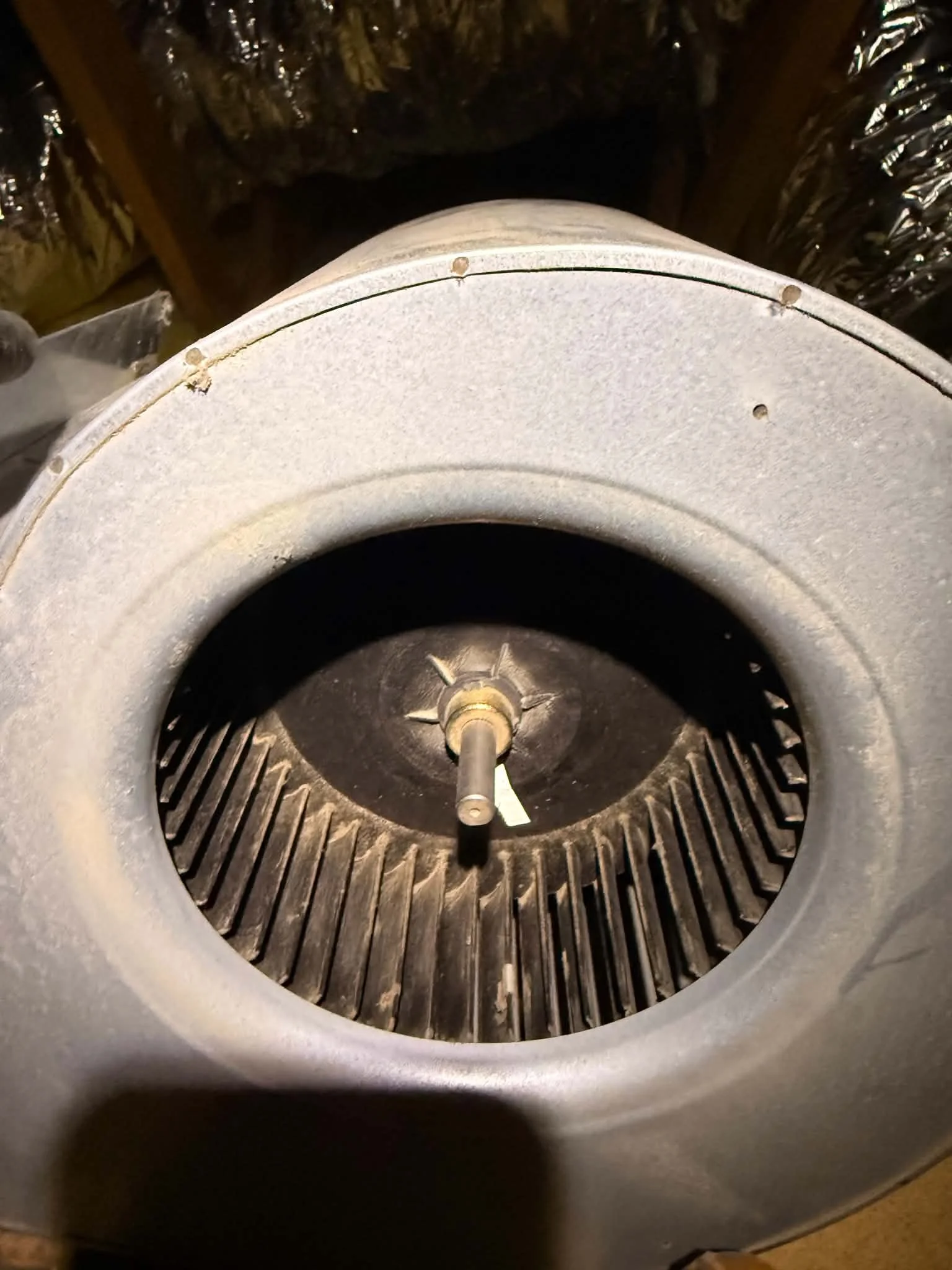 Interior view of a large industrial fan or blower with metal blades, viewed from above, with a circular opening and wiring attached.