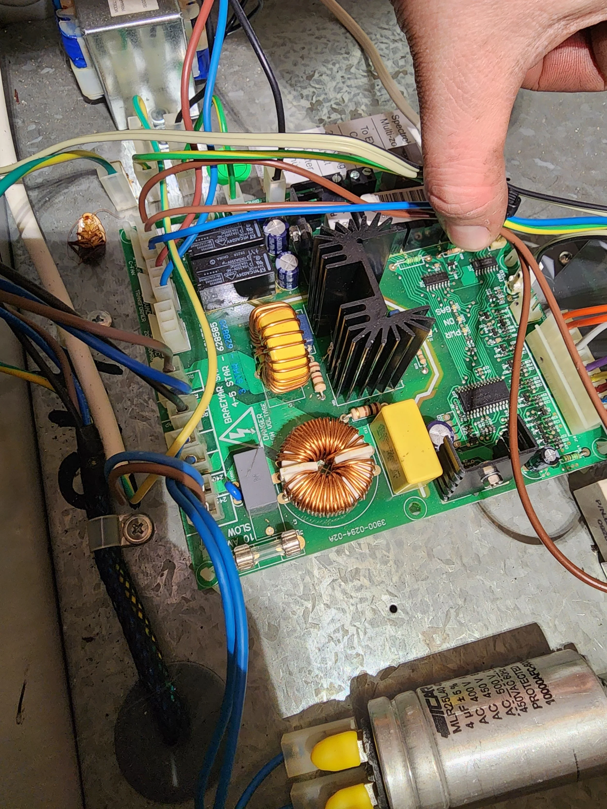 Close-up of electronic circuitry with wires, a circuit board, and electronic components mounted on a metal surface, including a capacitor and inductors.