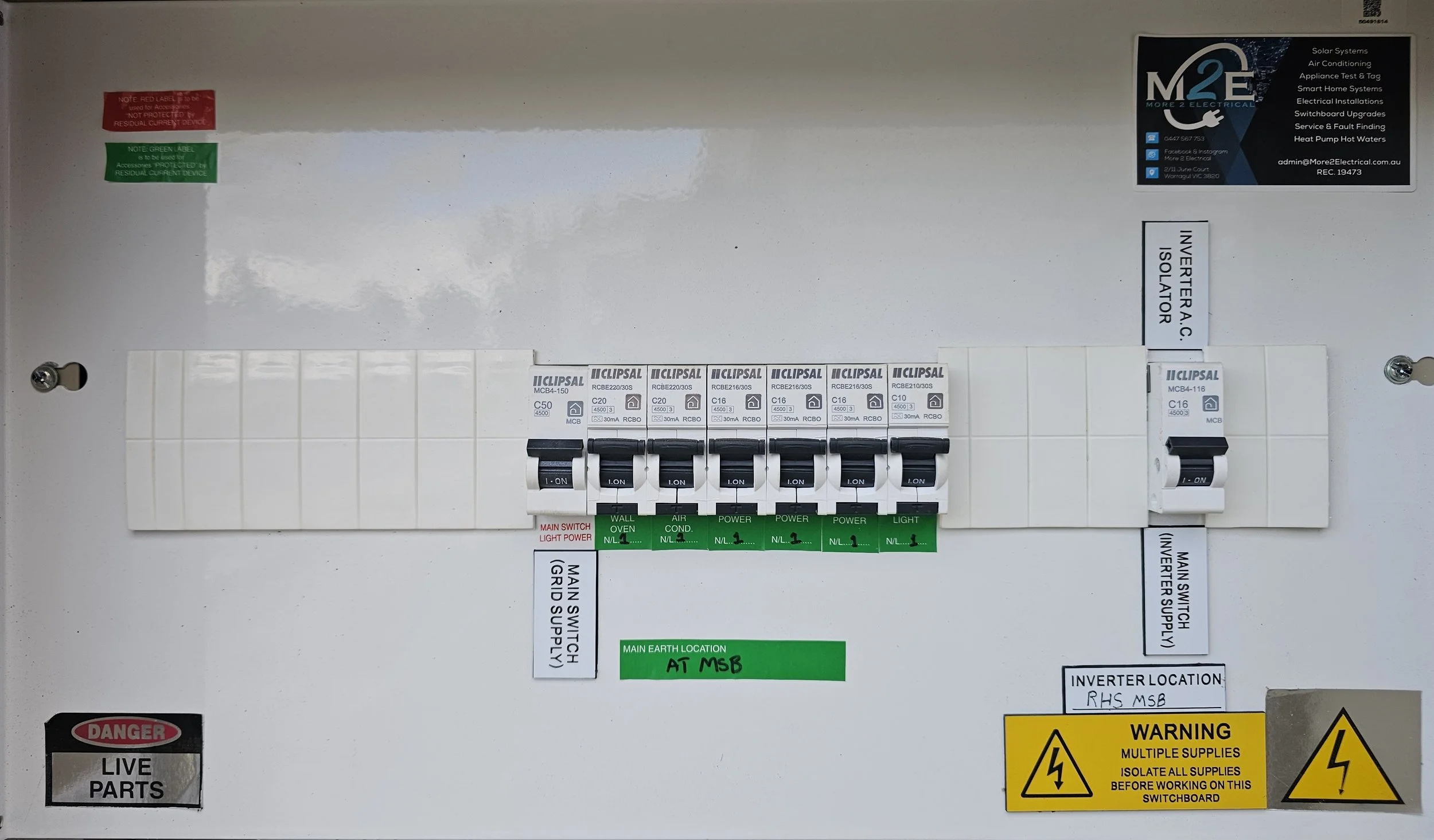 Electrical control panel with circuit breakers labeled for various functions such as main switch, wall oven, air conditioning, power, and light. Several warning and informational stickers are visible, including dangers and instructions for safety and maintenance.