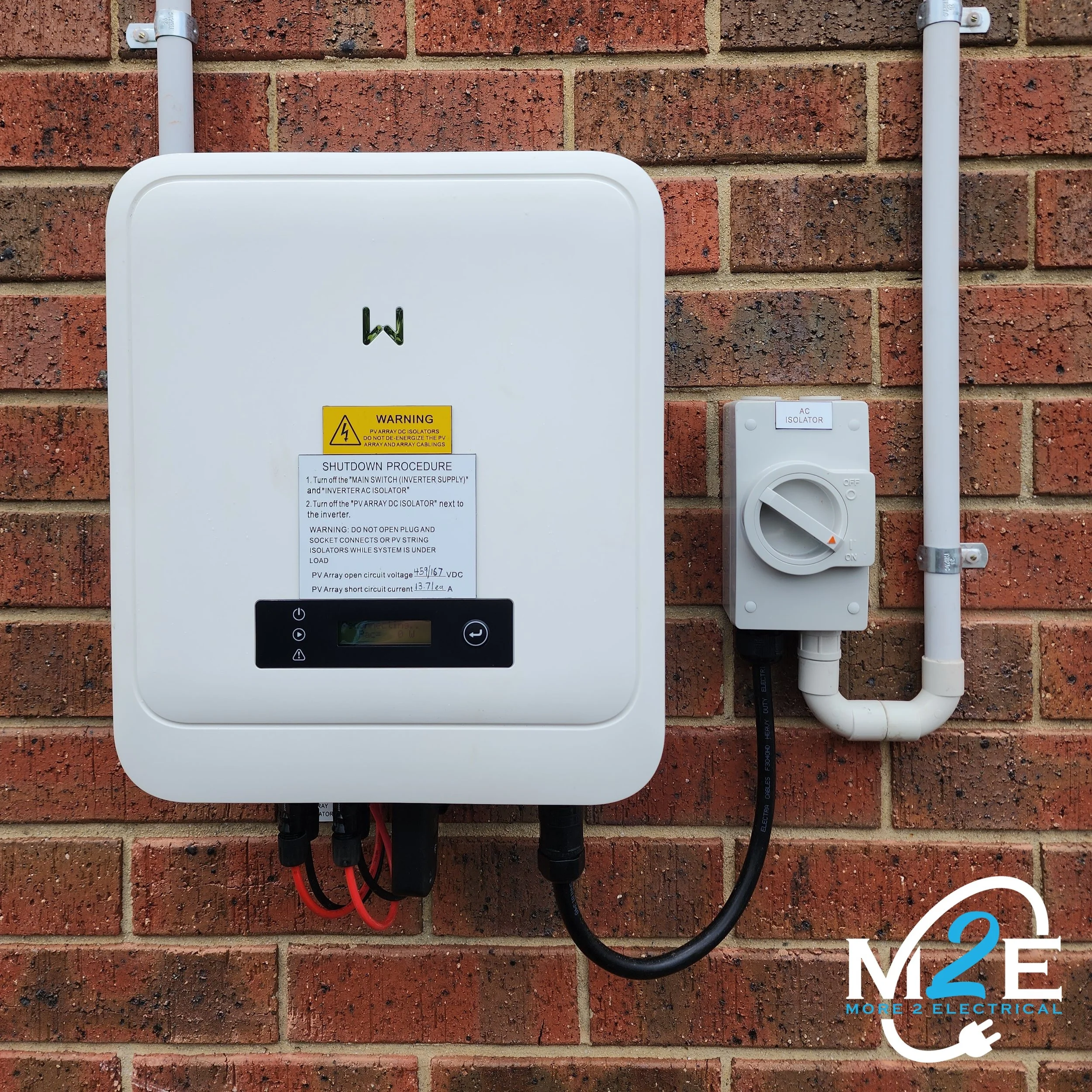 Electrical inverter mounted on a brick wall with incoming and outgoing wires connected, labeled for shutdown procedure.