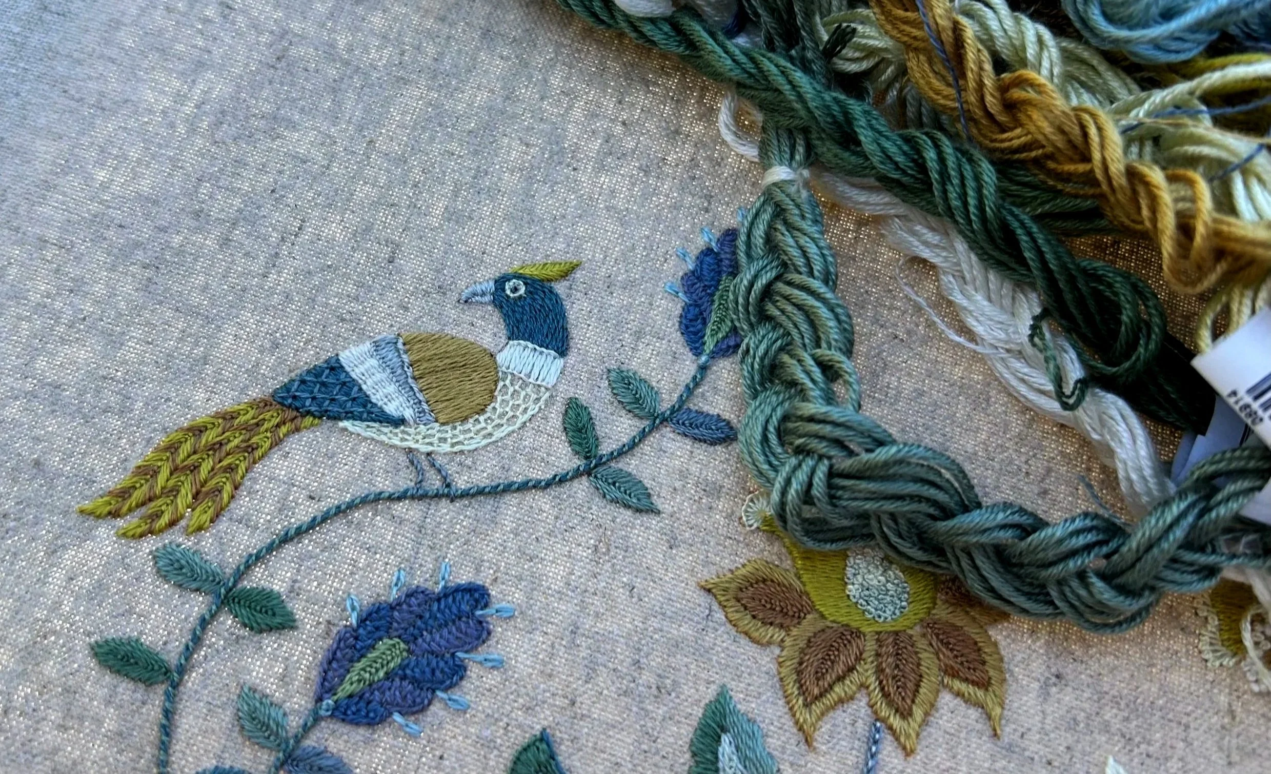 Progress picture of silk embroidred bird. Skeins of thread draped across the work.