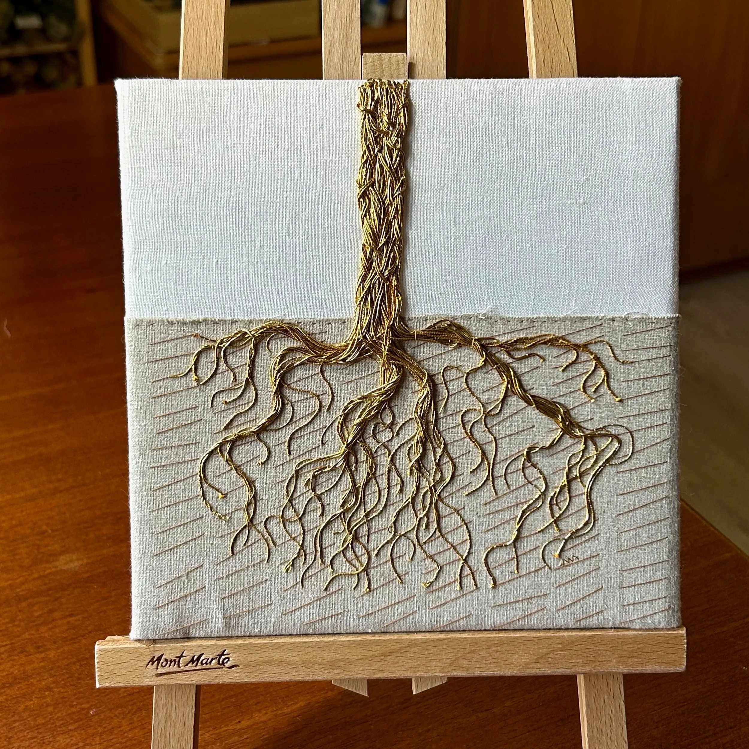 Goldwork thread embroidery of a gnarly tree trunk and roots under grounds. by Anna Scott