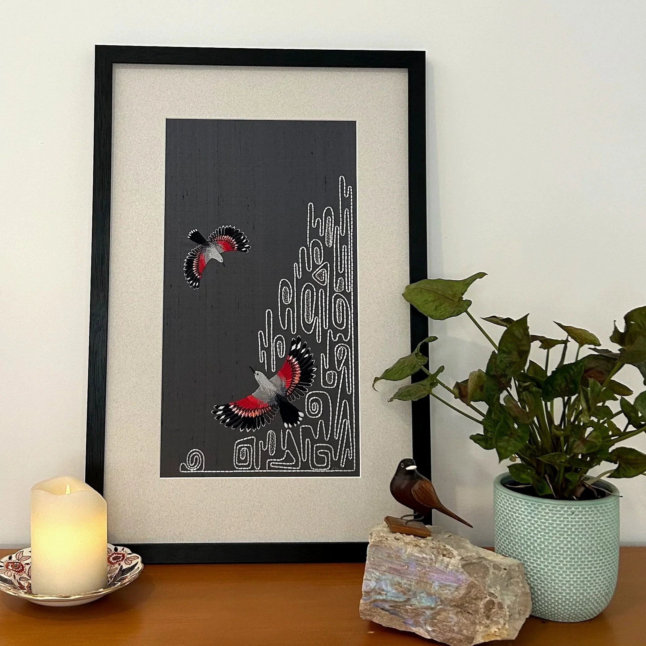 Silk embroidery panel featuring pair of birds in flight over a stylized mountainside. The background is slate-blue silk and the birds are black, grey and white with scarlet wings. The mountain is metallic silver and beads.